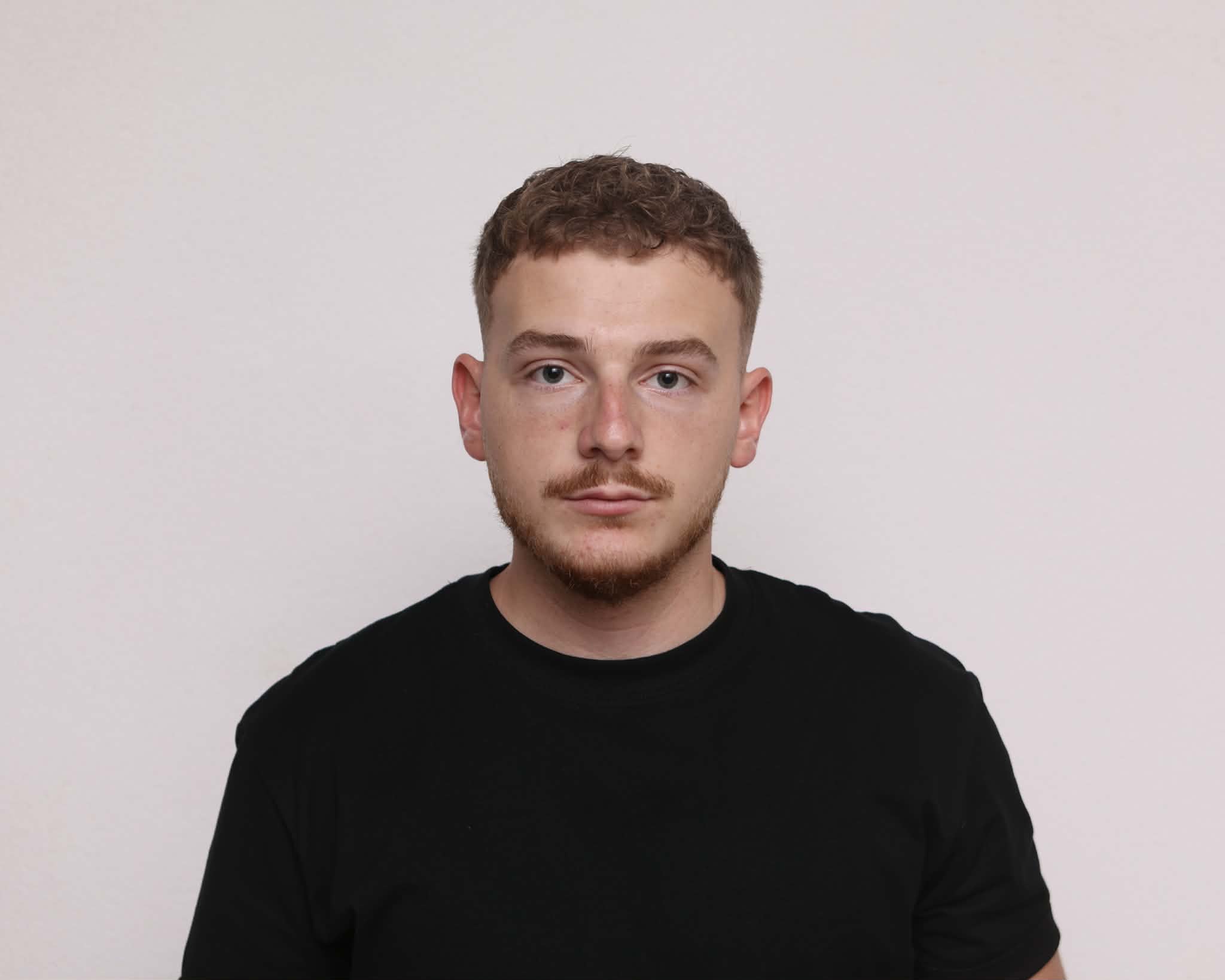 Person centered against a pale background wearing a black t-shirt, facing the camera with a neutral posture; facial area is intentionally blurred; overall tone calm and neutral